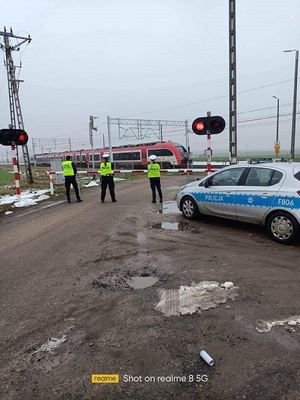 policjanci i straż ochrony kolei monitorują bezpieczeństwo przed przejazdem kolejowym.