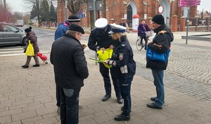 POLICJANCI ROZDAJĄ ELEMENTY ODBLASKIWE PIESZYM UCZESTNIKOM RUCHU DROGOWEGO.