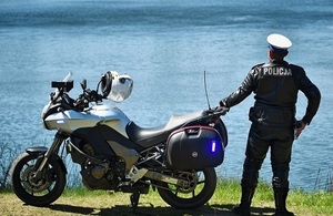 policjant ruchu drogowego z motocyklem służbowym na tle jeziora.