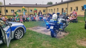 radiowóz i motocykl policyjny , w tle siedzące dzieci.