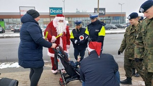 Mikołaj dzieciom rozdaje odblaski,, obok policjanci, żołnierze.