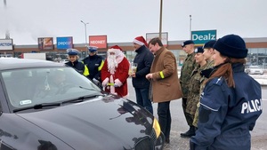 Mikołaj rozdaje odblaski, obok samochód, policjanci i żołnierze.