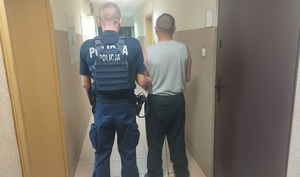 policjant prowadzi zatrzymanego mężczyznę korytarzem jednostki.