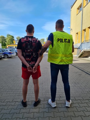 policjant prowadzi zatrzymanego mężczyznę.