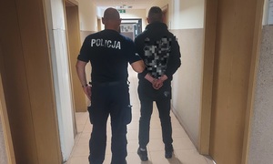policjant prowadzi zatrzymanego mężczyznę korytarzem komendy.