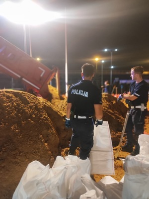 policjanci pomagają napełniać worki piaskiem.