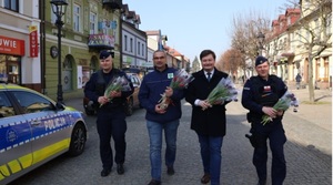 policjanci wraz z Starostą kutnowskim oraz członkiem zarządu powiatu kutnowskiego rozdaja kwiaty kobietom.