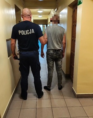 policjant prowadzi zatrzymanego mężczyznę.