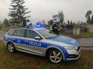 policjant stojący przy radiowozie w rejonie cmentarza.