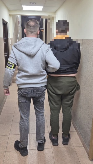 policjant prowadzi zatrzymanego mężczyznę.