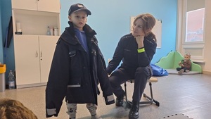 policjantka z chłopcem z przedszkola ubranym w kurtkę policyjną.