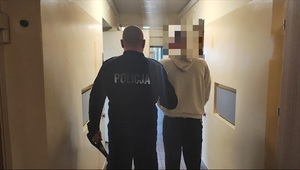 policjant prowadzi zatrzymanego mężczyznę.