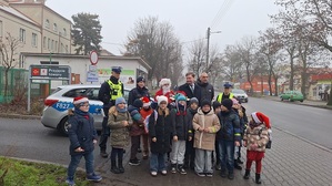 Policjanci z Mikołajem wraz z grupą dzieci na tle radiowozu.