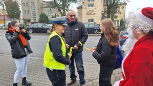 Policjanci z Mikołajem przekazują grupie dzieci elementy odblaskowe.