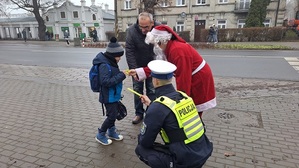 Policjanci z Mikołajem przekazuje dziecku elementy odblaskowe.