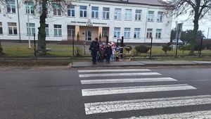 policjantka przeprowadza dzieci przez oznakowane przejście dla pieszych w rejonie szkoły.