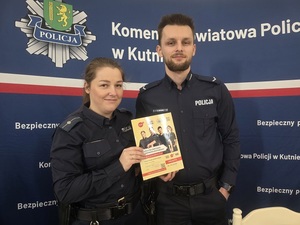Policjantka i policjant stoją na tle napisu Komenda Powiatowa Policji w Kutnie.