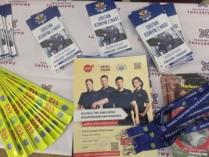 Ulotki i gazetki o tematyce policyjnej wraz z elementami odblaskowymi leżą na ławce.