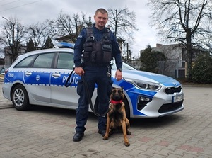 policjant wraz z pieskiem - Walutą na tle radiowozu .