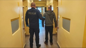 policjant prowadzi zatrzymanego mężczyznę.