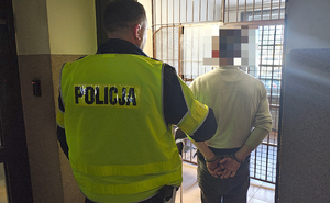 policjant prowadzi zatrzymanego mężczyznę.