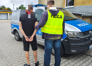 policjant prowadzi zatrzymanego mężczyznę.