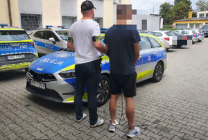 policjant prowadzi zatrzymanego mężczyznę do radiowozu.