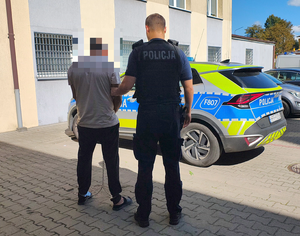 policjant prowadzi zatrzymanego mężczyznę do radiowozu.